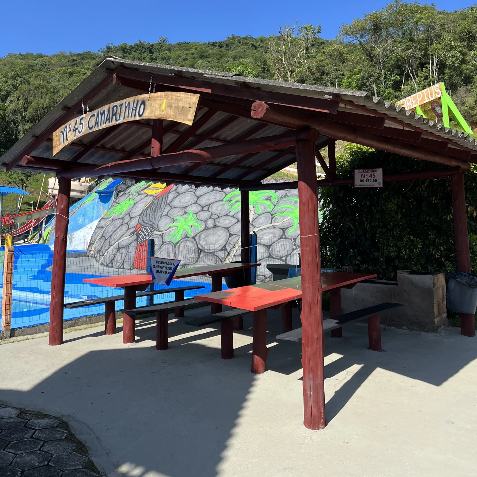 Espaço coberto com mesa, bancos e churrasqueira.